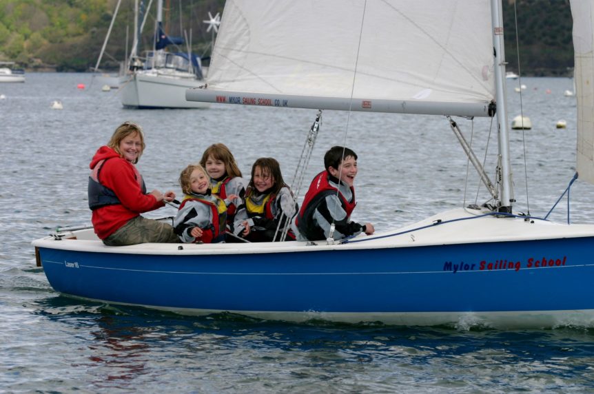 An instructor and 4 children sailing a dinghy having fun at mylor sailing school falmouth