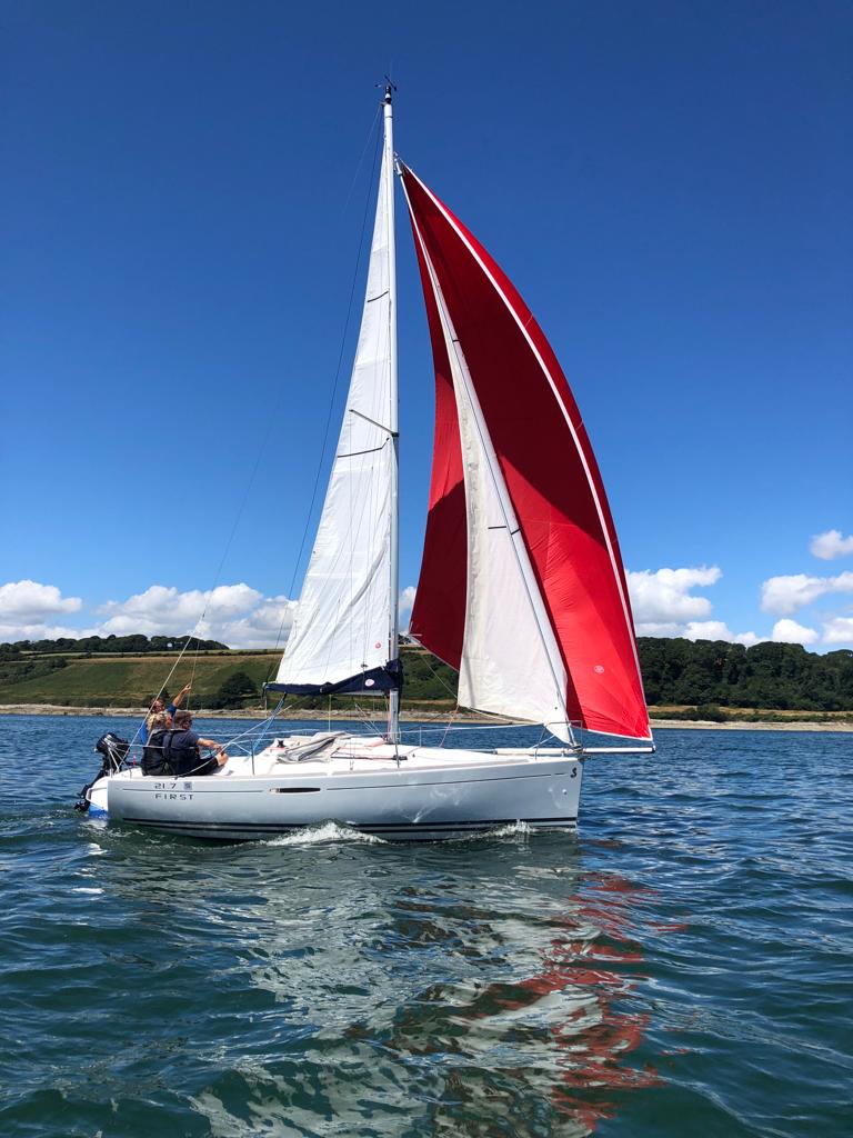 Beneteau First keelboat sailing with red spinnaker and two adults onboard on a lovely sunny day