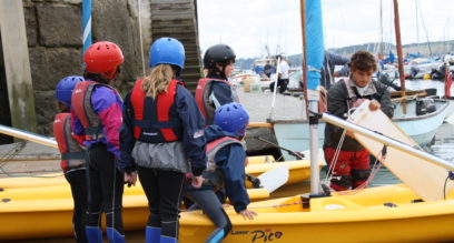 Group of children launching their boats at a slipway at Mylor Sailing School in Cornwall