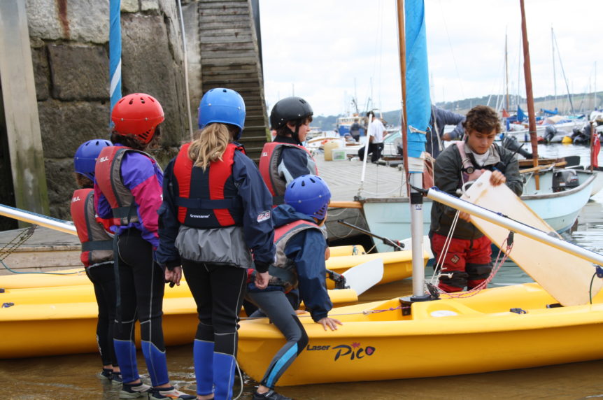 Group of children launching their boats at a slipway at Mylor Sailing School in Cornwall