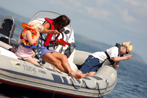 Mother and two young children crabbing from a small motorboat on a sunny day at Mylor Sailing School near Falmouth, Cornwall