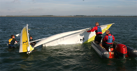 Two young adults rescuing a sailing dinghy from a capsize with two sailors in the water at Mylor Sailing School near Falmouth, Cornwall