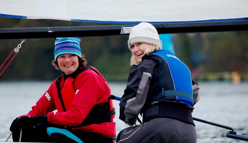 Two ladies smiling sailing a small dinghy at Mylor Sailing School near Falmouth Cornwall