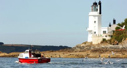 Small red boat motoring past St Anthony's light house at Mylor Sailng School near Falmouth, Cornwall