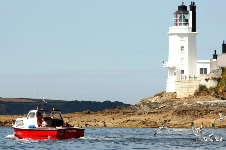 Small red boat motoring past St Anthony's light house at Mylor Sailng School near Falmouth, Cornwall