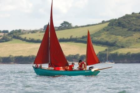 family sailing in a blue boat with red sail at mylor sailing school near Falmouth