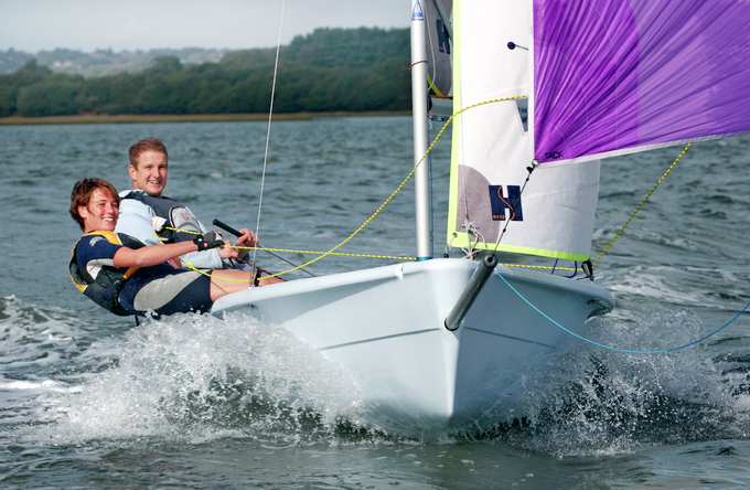 A man and a lady sailing fast with a purple spinnaker sail at mylor Sailing School in falmouth, Cornwall