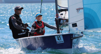 Two adults sailing a Laser 2000 dinghy with blue spinnaker sail at Mylor Sailing School near Falmouth, Cornwall