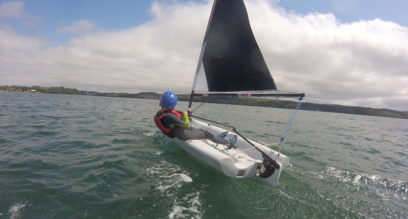 Young boy sailing a small dinghy with helmet on a sunny day at Mylor Sailing School near Falmouth, Cornwall