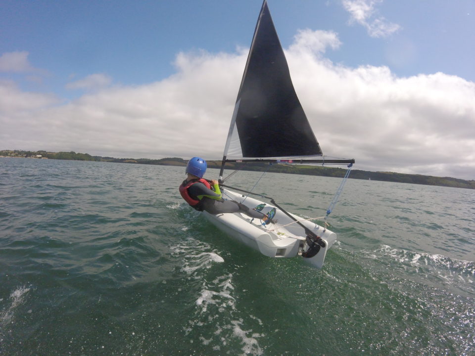 Young boy sailing a small dinghy with helmet on a sunny day at Mylor Sailing School near Falmouth, Cornwall