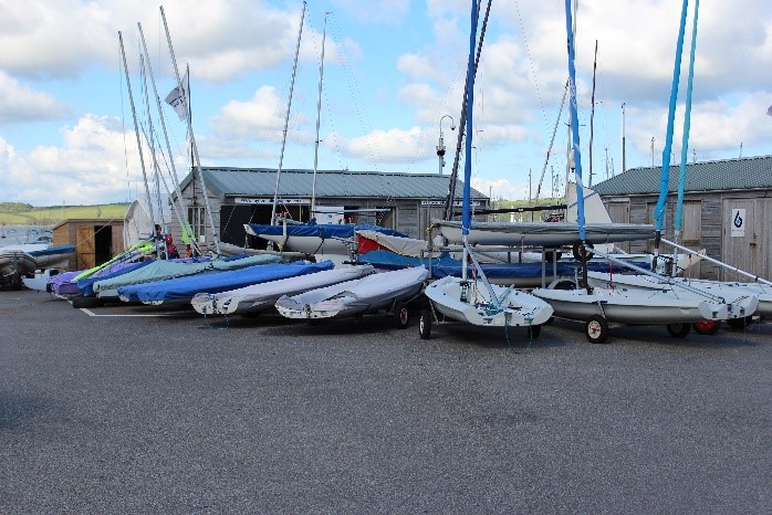 Large level area with sailing dinghies parked outside wooden huts at Mylor Sailing School