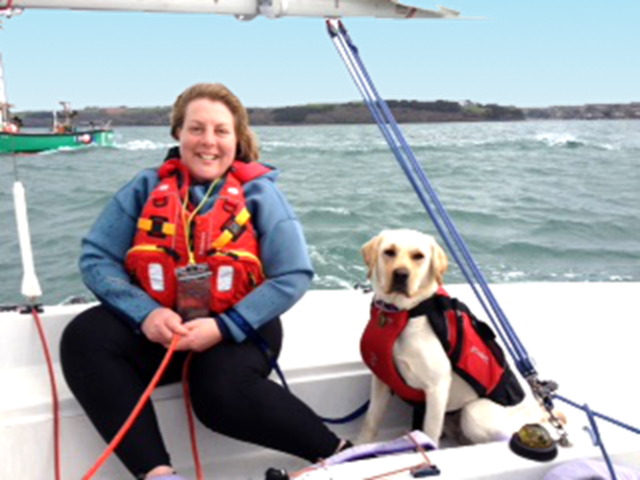 Lady sailing a dinghy with assistance dog at Mylor Sailing School Falmouth Cornwall