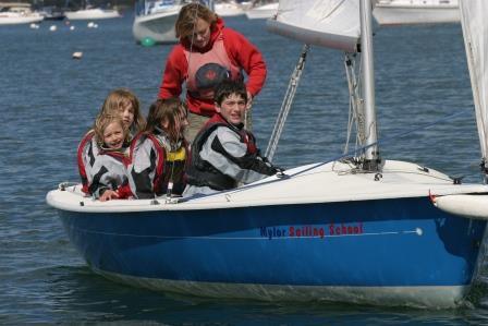 Female instructor and group of four children sailing together in a blue dinghy at Mylor Sailing School Falmouth Cornwall