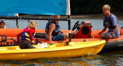 2 instructors teaching a child to sail from a rescue boat at Mylor Sailing School in Falmouth Cornwall