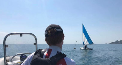 The back of a sailing instructor teaching 1 person in a Pico dinghy from a RIB at Mylor Sailing School Falmouth Cornwall