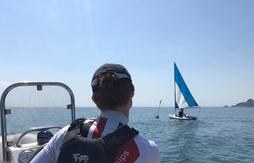 The back of a sailing instructor teaching 1 person in a Pico dinghy from a RIB at Mylor Sailing School Falmouth Cornwall