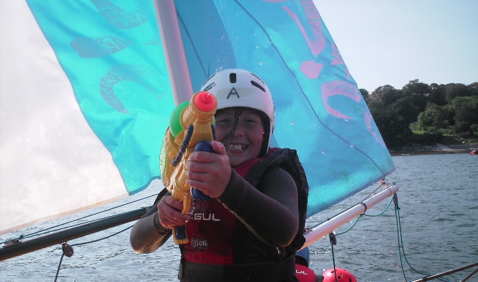 young girl with water pistol on a sailing dinghy having fun at Mylor Sailing School Falmouth Cornwall