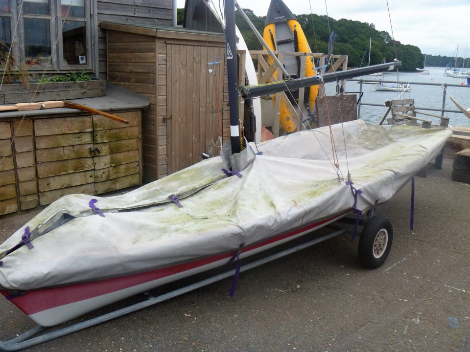 small sailing dinghy with cover on at mylor sailing school falmouth