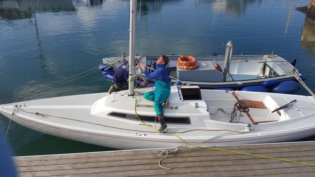 person helping to rig the mast on H Boat alongside pontoon at Mylor Sailing School Falmouth Cornwall