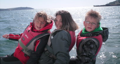 Three children sailing on a keelboat in sunny Falmouth at Mylor Sailing and Powerboat School Falmouth Cornwall
