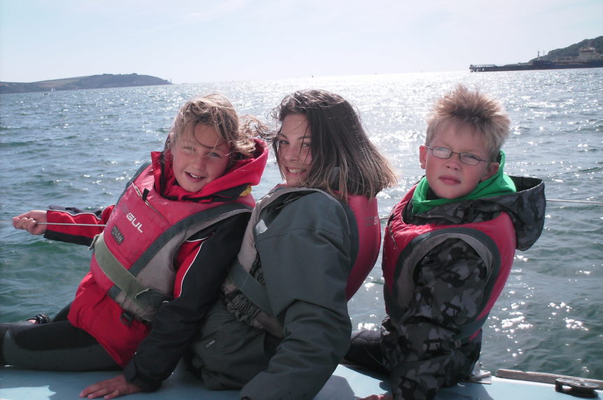 Three children sailing on a keelboat in sunny Falmouth at Mylor Sailing and Powerboat School Falmouth Cornwall