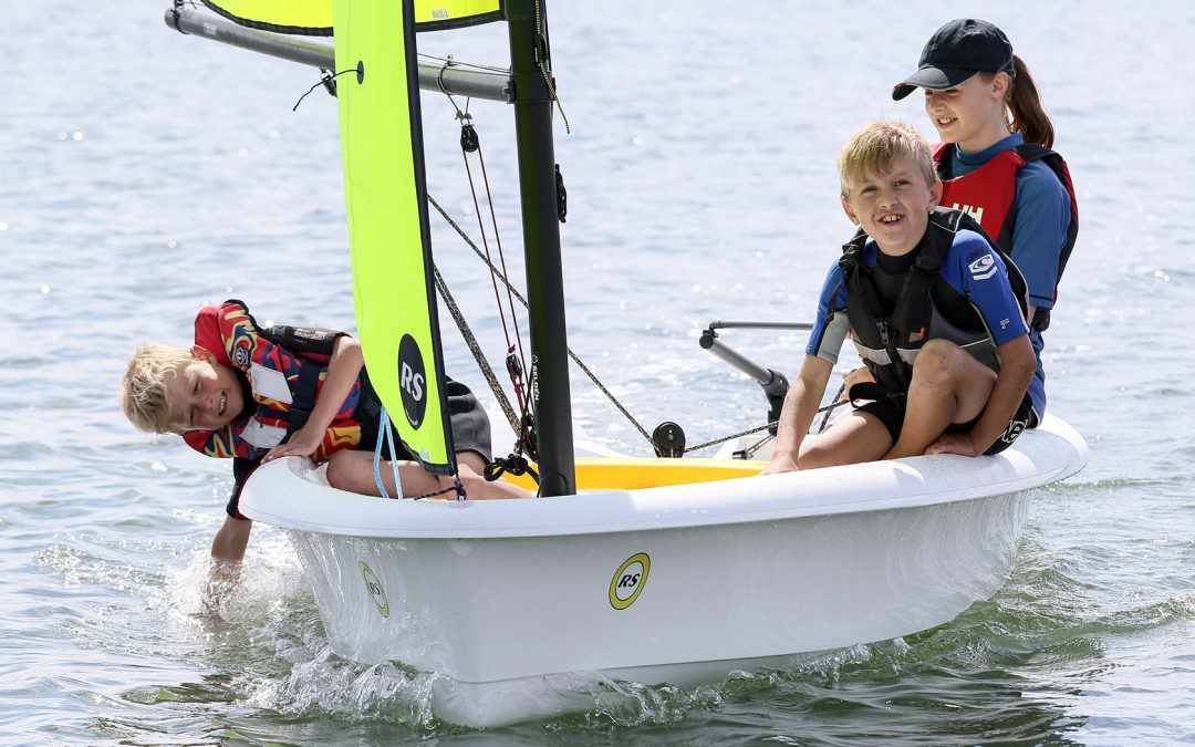 white plastic small sailing dinghy with three children sailing