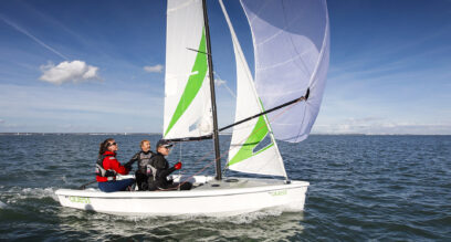white plastic sailing dinghy with 3 people flying the spinnaker