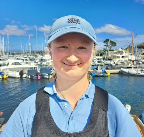 teenage girl caucasian, wearing a blue cap smiling with a background of sailing boats
