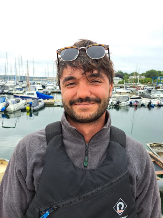 young man smiling with sunglasses on his head with a background of boats at Mylor Sailing School Falmouth Cornwall