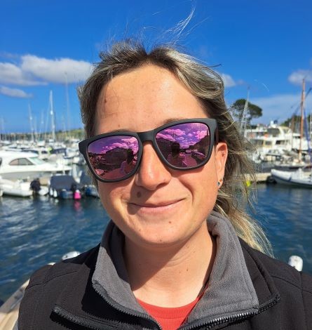Female in her 20s wearing sunglasses on a sunny day with a background of boats.